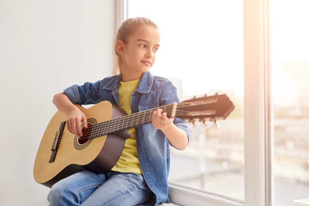 Girl playing guitar near window