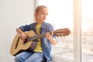 Girl playing guitar near window