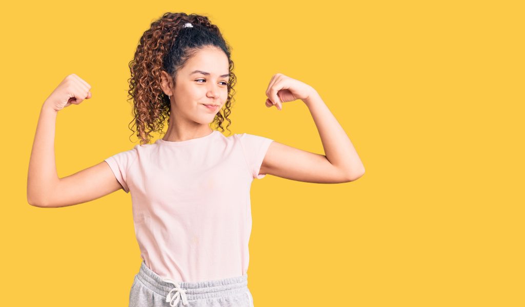 Beautiful kid girl with curly hair wearing casual clothes showing arms muscles smiling proud. fitness concept. girl with strong body